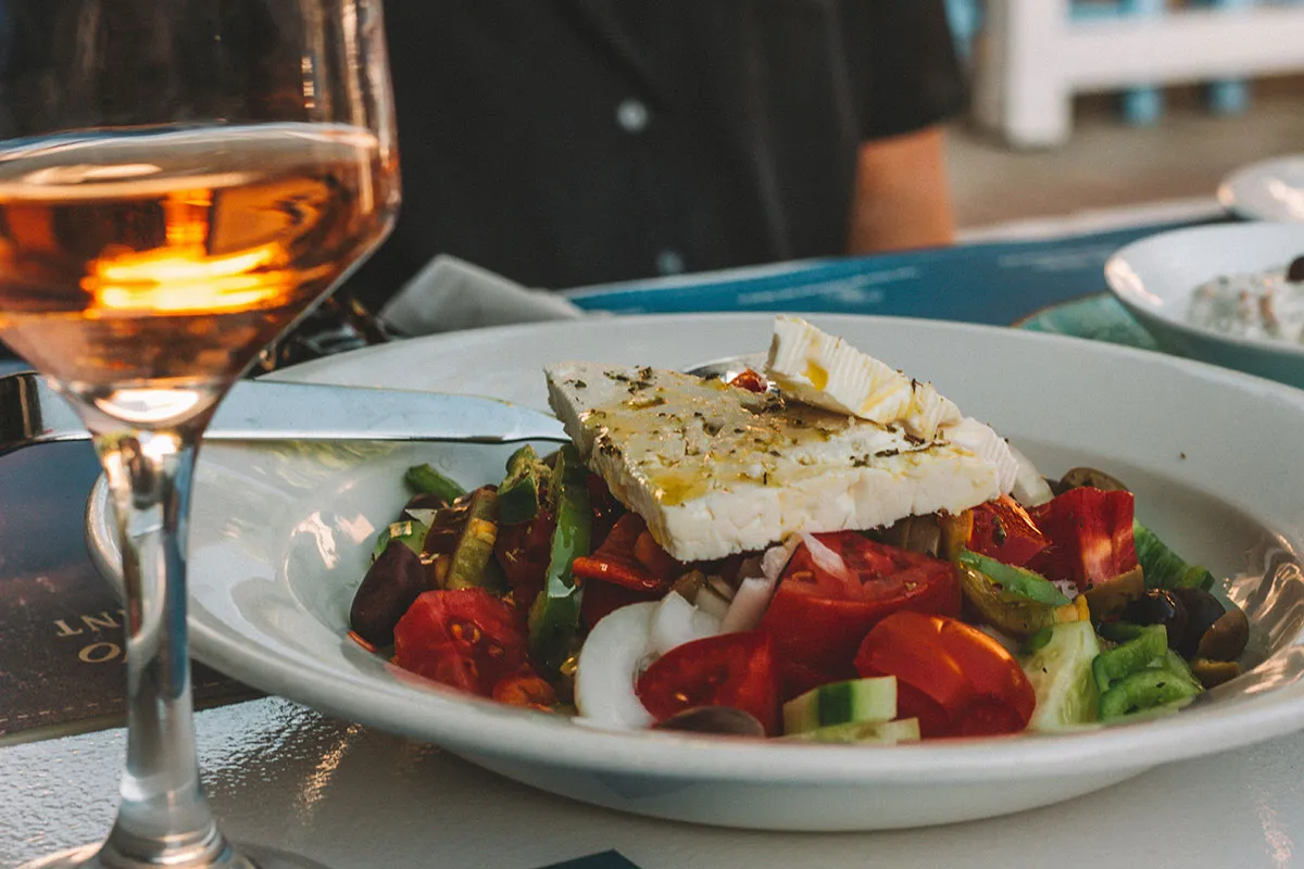 A Greek salad topped with feta, beside a glass of rosé