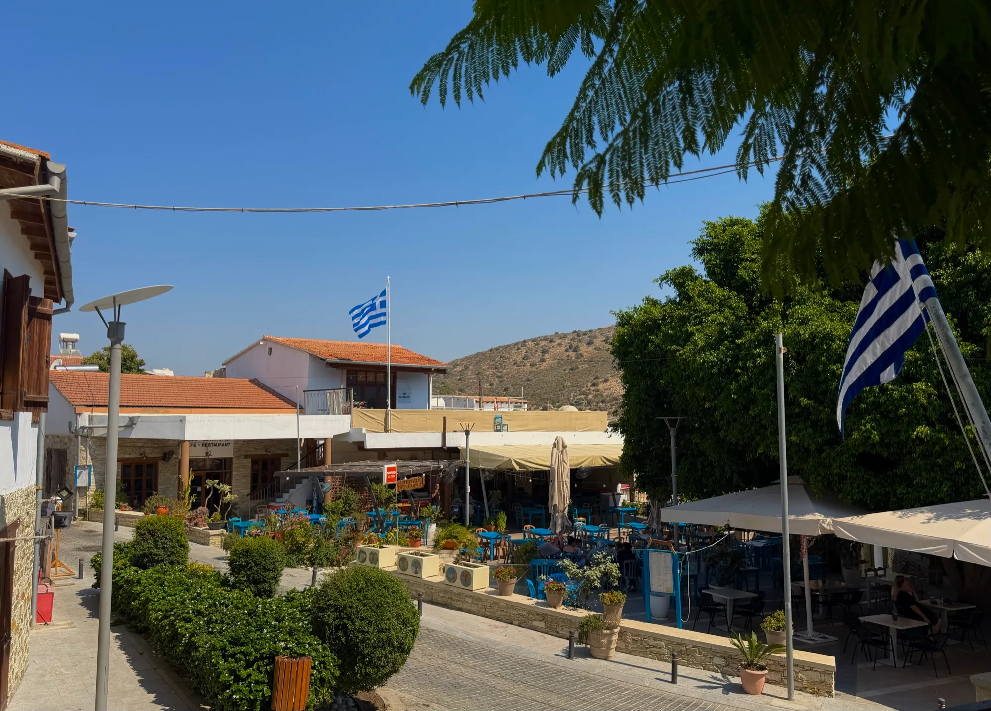 The village square with a Greek flag and hills beyond